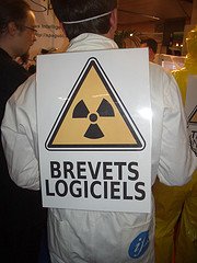 Libriste en combinaison blanche de peintre avec dans le dos un signe nucléaire avec inscrit en dessous : Brevets Logiciels